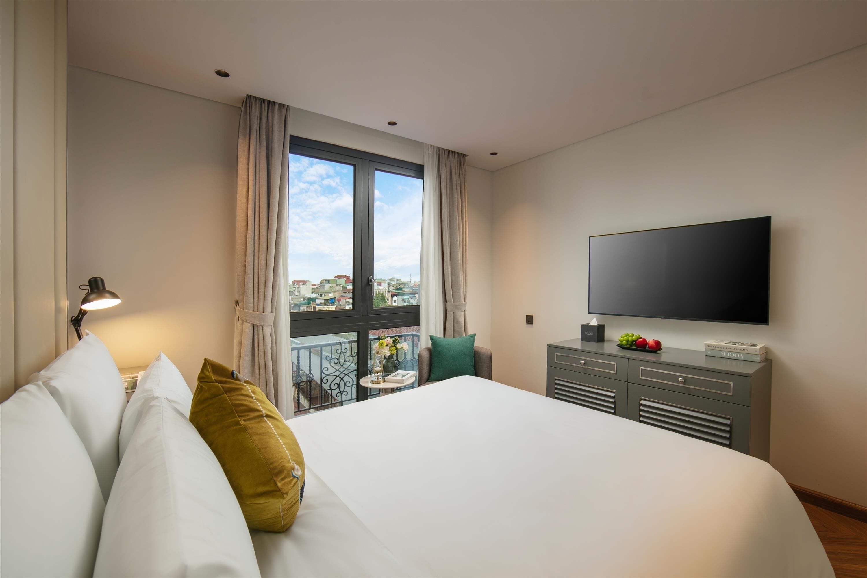 Habitación de hotel con una cama grande, un televisor de pantalla plana, un escritorio con lámpara y un balcón con vista a la ciudad.