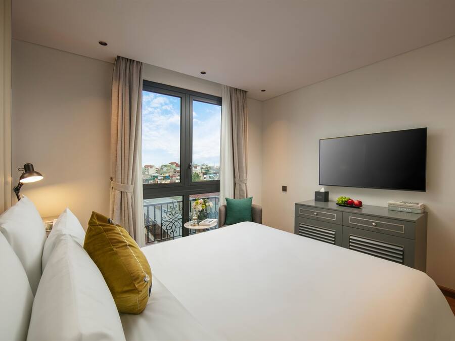 Habitación de hotel con una cama grande, un televisor de pantalla plana, un escritorio con lámpara y un balcón con vista a la ciudad.