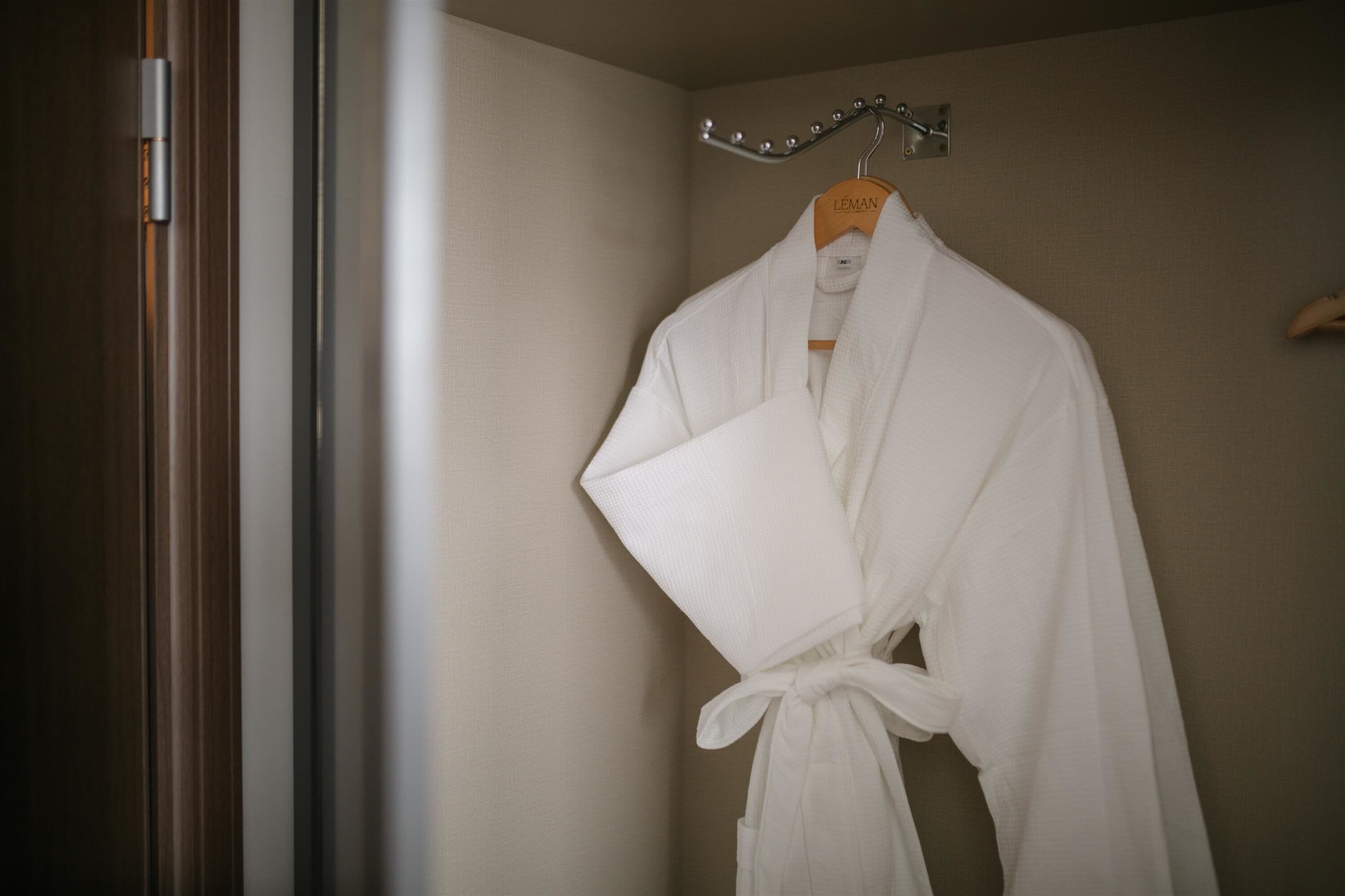 A white robe hanging on a wooden hanger in a bathroom with a wooden door and beige walls.