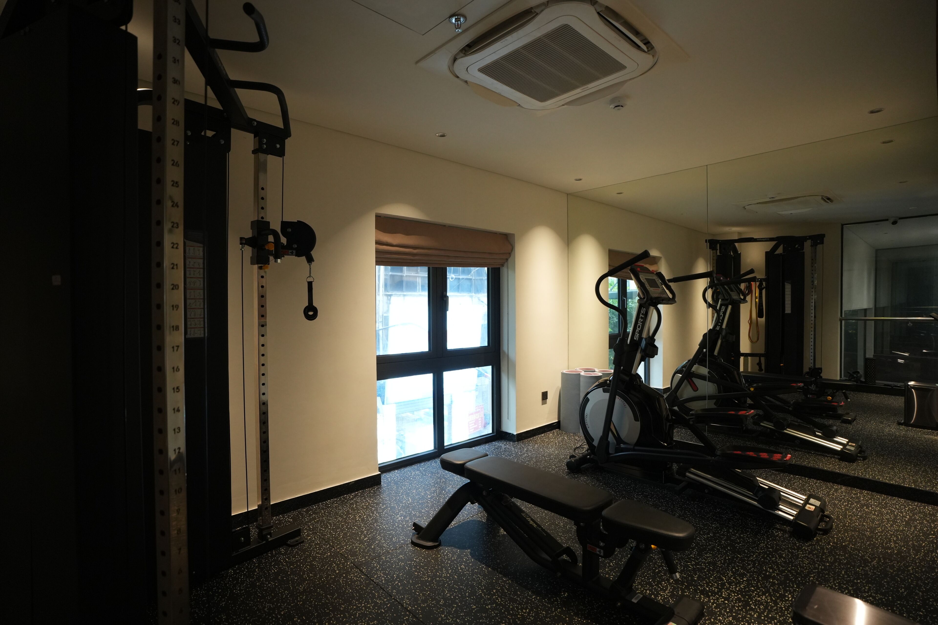 A gym with exercise equipment, a bench, and a window with blinds.