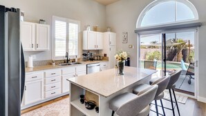A modern kitchen with white cabinets, a large island with bar stools, and a view of a backyard with a pool.