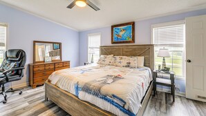 Ein Schlafzimmer mit Bett, Stuhl, Kommode, Deckenventilator und Fenster mit Jalousien.