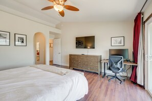 Une chambre avec un grand lit, une commode en bois, un bureau avec une chaise, un ventilateur de plafond et des œuvres d’art accrochées aux murs.