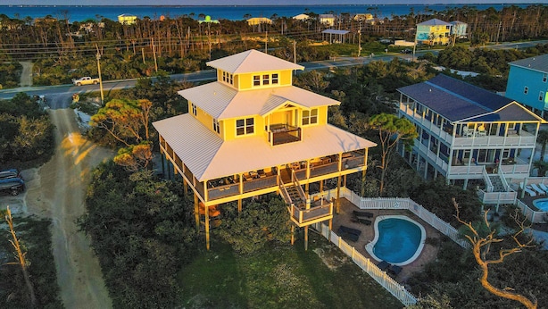 Uma casa grande e de vários andares com uma varanda saliente, uma piscina e vista para o oceano.