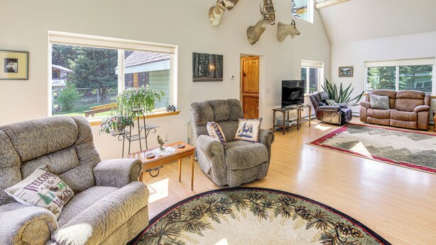 A spacious living room with a high ceiling, a fireplace, and a large window overlooking a garden. - Private Hot Tub: 'Enchanted Hideaway' in Lincoln! (Lincoln)