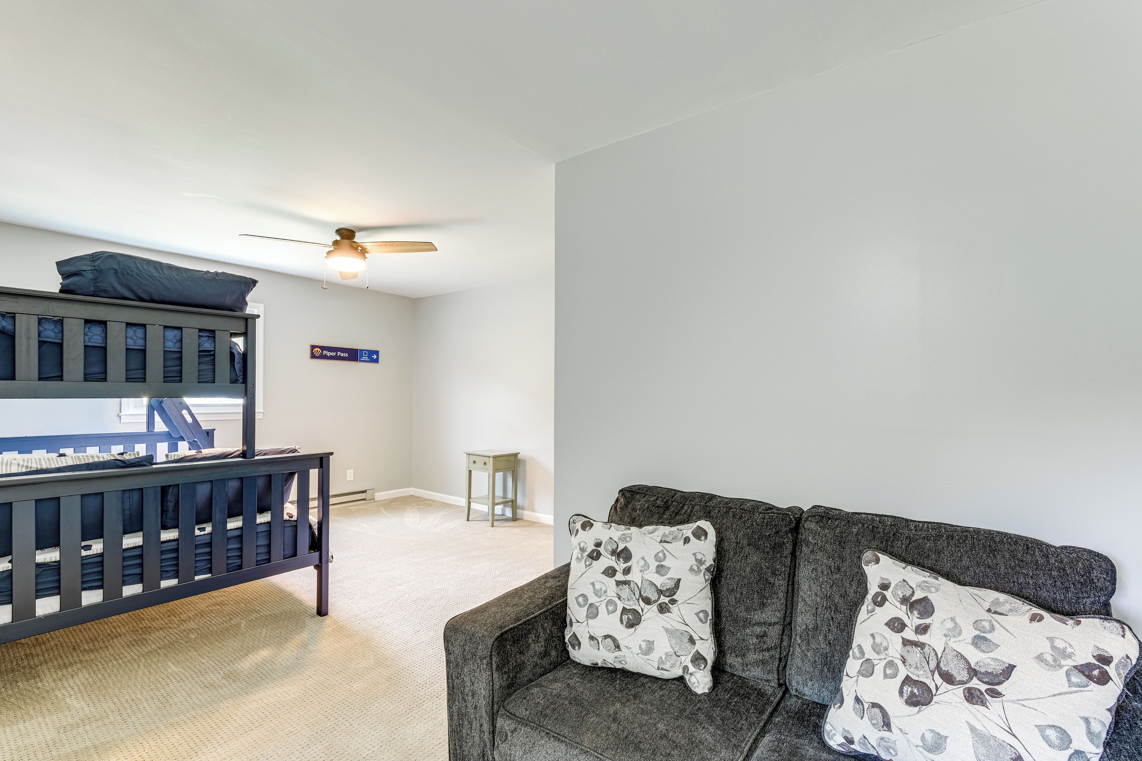 Une pièce avec un lit superposé, une petite table, un canapé avec des coussins à motifs et un ventilateur de plafond.