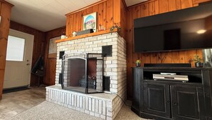 A living room with a brick fireplace, a flat-screen TV mounted on the wall, and a black entertainment unit.