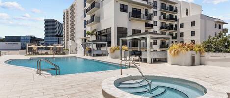 Un hôtel moderne doté d’un espace piscine sur le toit, comprenant un jacuzzi circulaire et une piscine classique avec un plongeoir.