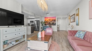 Ein modernes Wohnzimmer mit Fernseher, einem rosafarbenen Sofa, einem Couchtisch und einer K üche im Hintergrund.