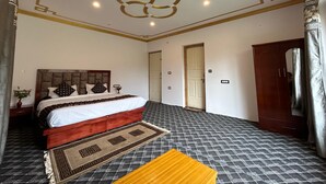A bedroom with a bed, a wooden headboard, a patterned rug, and a mirror. - Otsal Villa (Leh)