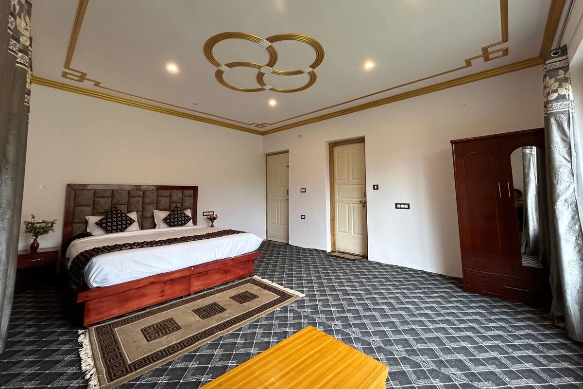 A bedroom with a bed, a wooden headboard, a patterned rug, and a mirror.