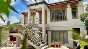 A multi-story building with a staircase, potted plants, and flags on the roof. - Otsal Villa (Leh)