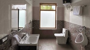 A bathroom with a bathtub, a toilet, and a shower. There is a window providing natural light. - Otsal Villa (Leh)