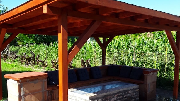 A covered outdoor seating area with a stone fireplace, wooden bench seating, and a small bar area. - Charming house in Tápiószentmárton (Tápiószentmárton)