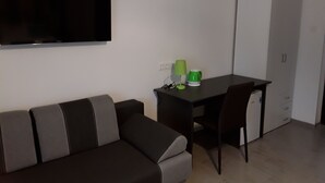 A modern living room with a sofa, a TV mounted on the wall, a desk with a lamp and a green mug, and a wardrobe. - Charming house in Tápiószentmárton (Tápiószentmárton)