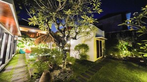 A well-lit garden area with a pathway, a small building, and various plants.