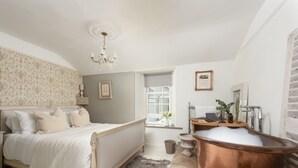Ein Schlafzimmer mit Bett, einer Kristallleuchter, einem Badezimmer mit Kupferbadewanne und einem Fenster mit Blick.