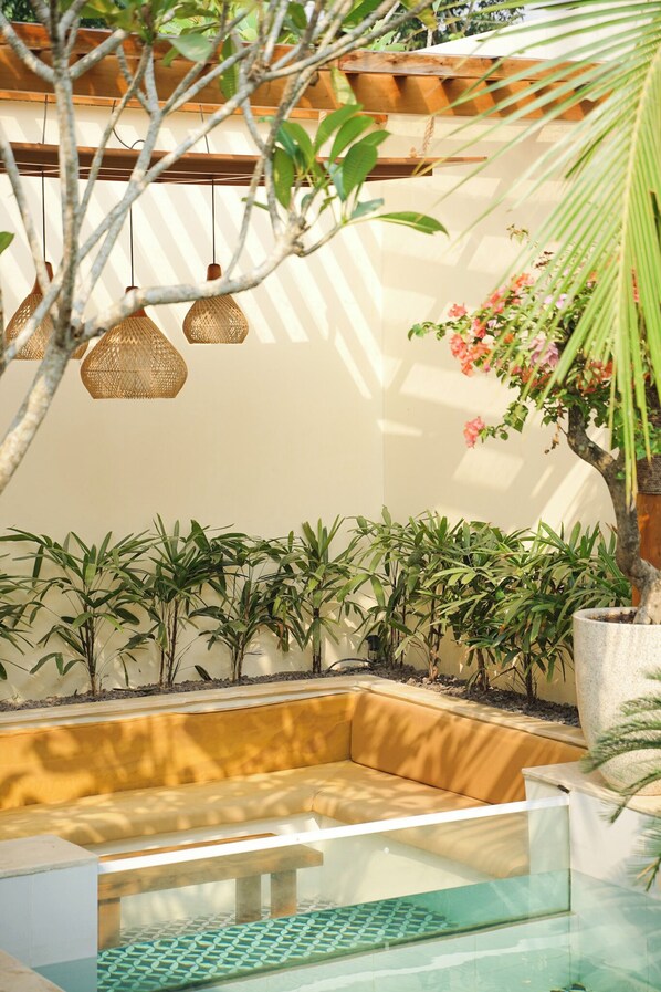 Un área de estar moderna al aire libre con una mesa de vidrio, rodeada de plantas en macetas y un banco de madera.