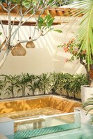 Un área de estar moderna al aire libre con una mesa de vidrio, rodeada de plantas en macetas y un banco de madera.