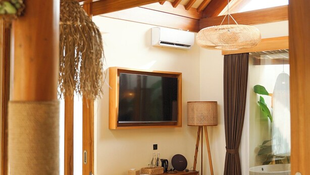 A wooden interior with a television, a rattan lamp, a glass door leading to a bathroom, and a woven mat on the floor. - Lavillas Jogja (Sleman)
