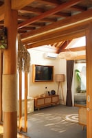 Un interior de madera con un televisor, una lámpara de ratán, una puerta de cristal que da a un baño y un tapete tejido en el suelo.