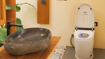 A bathroom with a stone basin, a toilet, a shower, and a wall-mounted air conditioning unit.