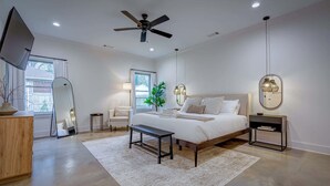 A modern bedroom with a large bed, bedside tables, a ceiling fan, and a view of the outside.