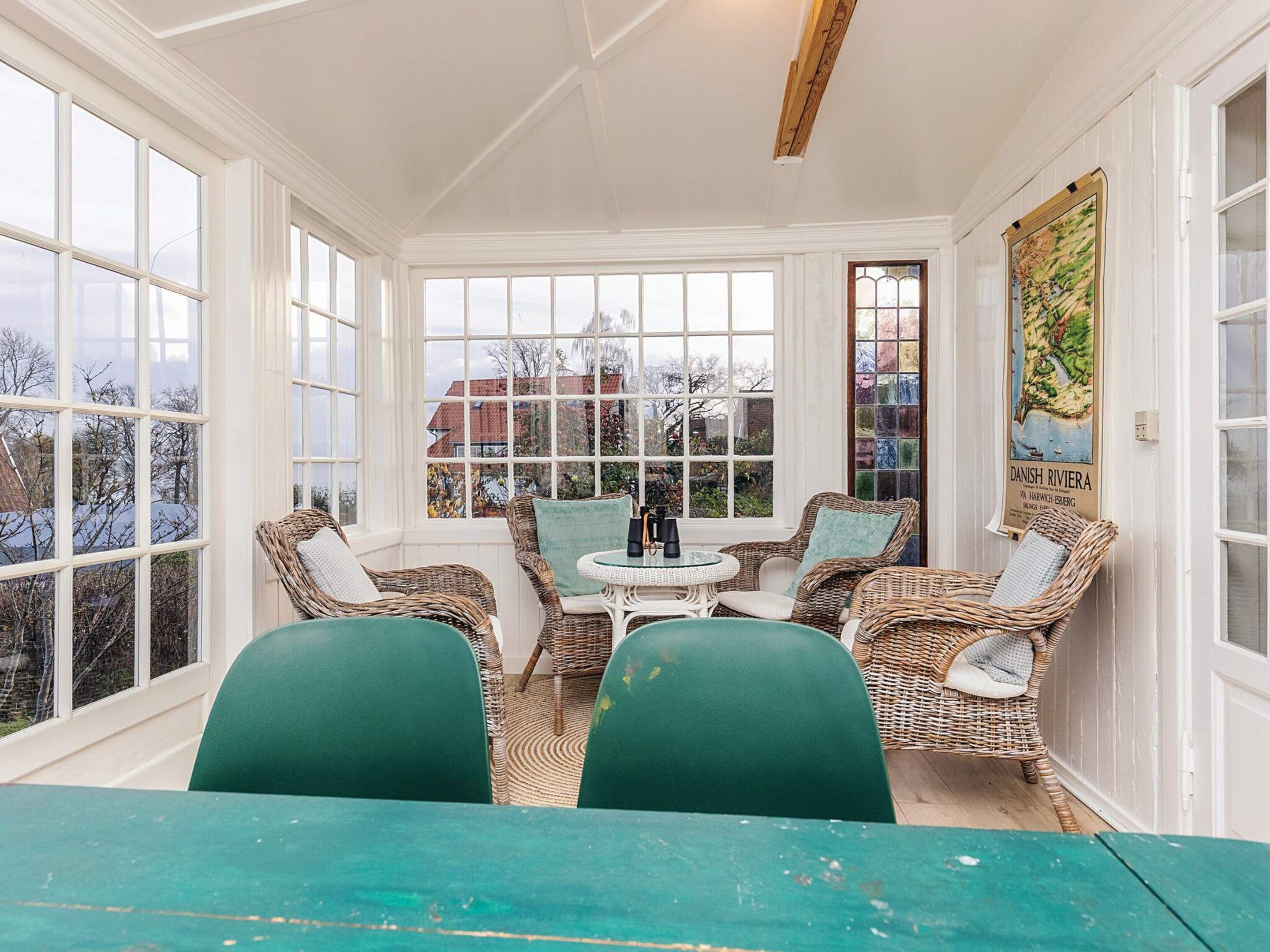 A sunroom with wicker furniture, a table, and large windows.