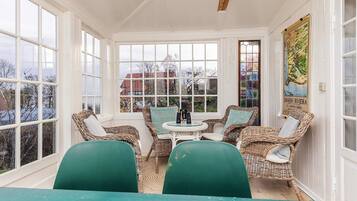 A sunroom with wicker furniture, a table, and large windows.