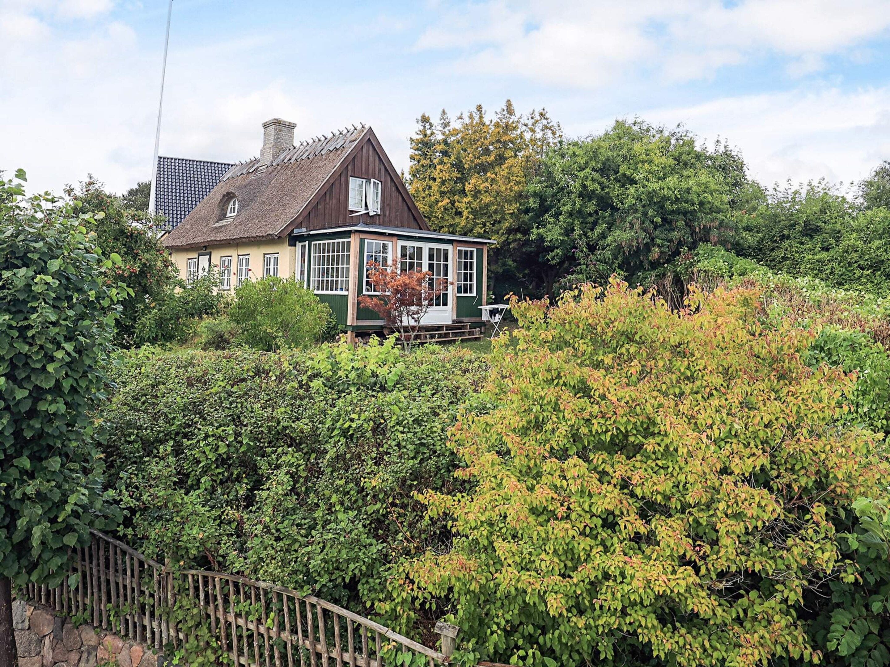 A house with a large garden, a wooden fence, and a thatched roof.