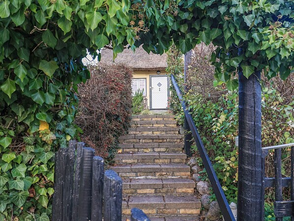A stone staircase leading to a door with a thatched roof, surrounded by greenery. - 4 Star Holiday Home in Humlebaek (Humlebaek)