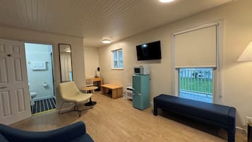 Et værelse med en blå sofa, et lille bord, en stol, et fjernsyn og et vindue med udsigt til en grøn græsplæne.