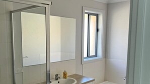 A bathroom with a white sink, a mirror, a window, and a bathtub. - Secure 4BR w/Garage Whyalla (Whyalla Jenkins)