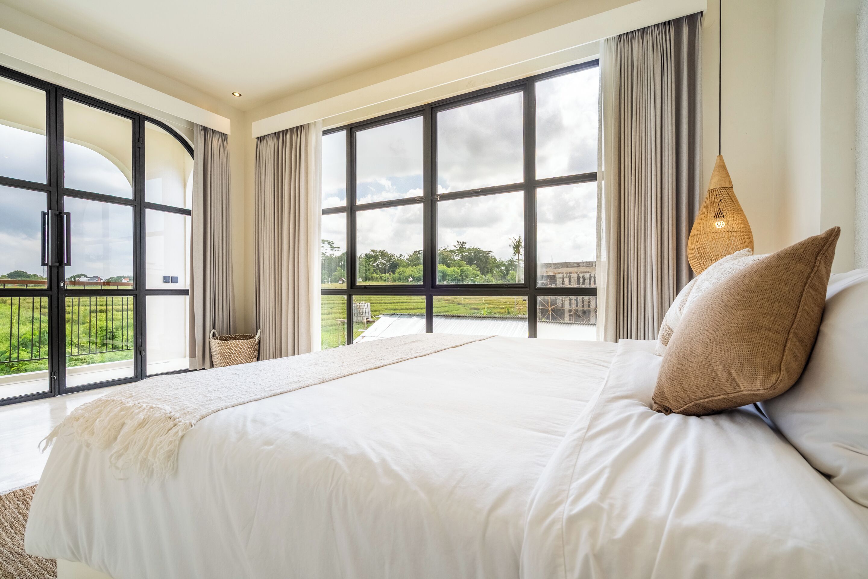 A spacious bedroom with a large bed, a view of a green landscape, and a large window with curtains.