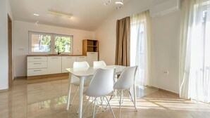 A modern kitchen with white cabinets, a dining table with chairs, and a window with curtains. - Adelsberg Inn by Interhome (Postojna)