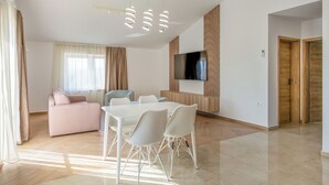 A modern living room with a sofa, dining table, chairs, and a TV mounted on a wooden panel wall. - Adelsberg Inn by Interhome (Postojna)