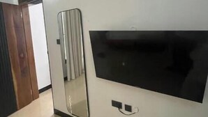 Una habitación con un espejo grande, un televisor negro fijado a la pared y una puerta de madera.