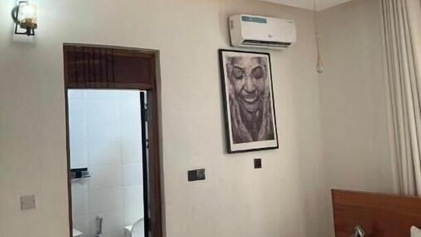 Habitación de hotel con cama, mesita de noche, aire acondicionado instalado en la pared, un cuadro enmarcado y un baño visible a través de una puerta abierta.