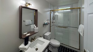 Un baño moderno con ducha de vidrio, un espejo grande y un tocador con lavabo y toallero.
