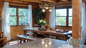 A wooden interior with a dining table, chairs, a chandelier, and a view of the outdoors. - Sleeps 22, 2 Homes | Theater Room, Game Room, Hot Tub, Smoky Mountain Views (Sevierville)