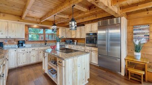 A wooden cabin-style kitchen with granite countertops, a central island, stainless steel appliances, and a wooden dining table. - Sleeps 22, 2 Homes | Theater Room, Game Room, Hot Tub, Smoky Mountain Views (Sevierville)