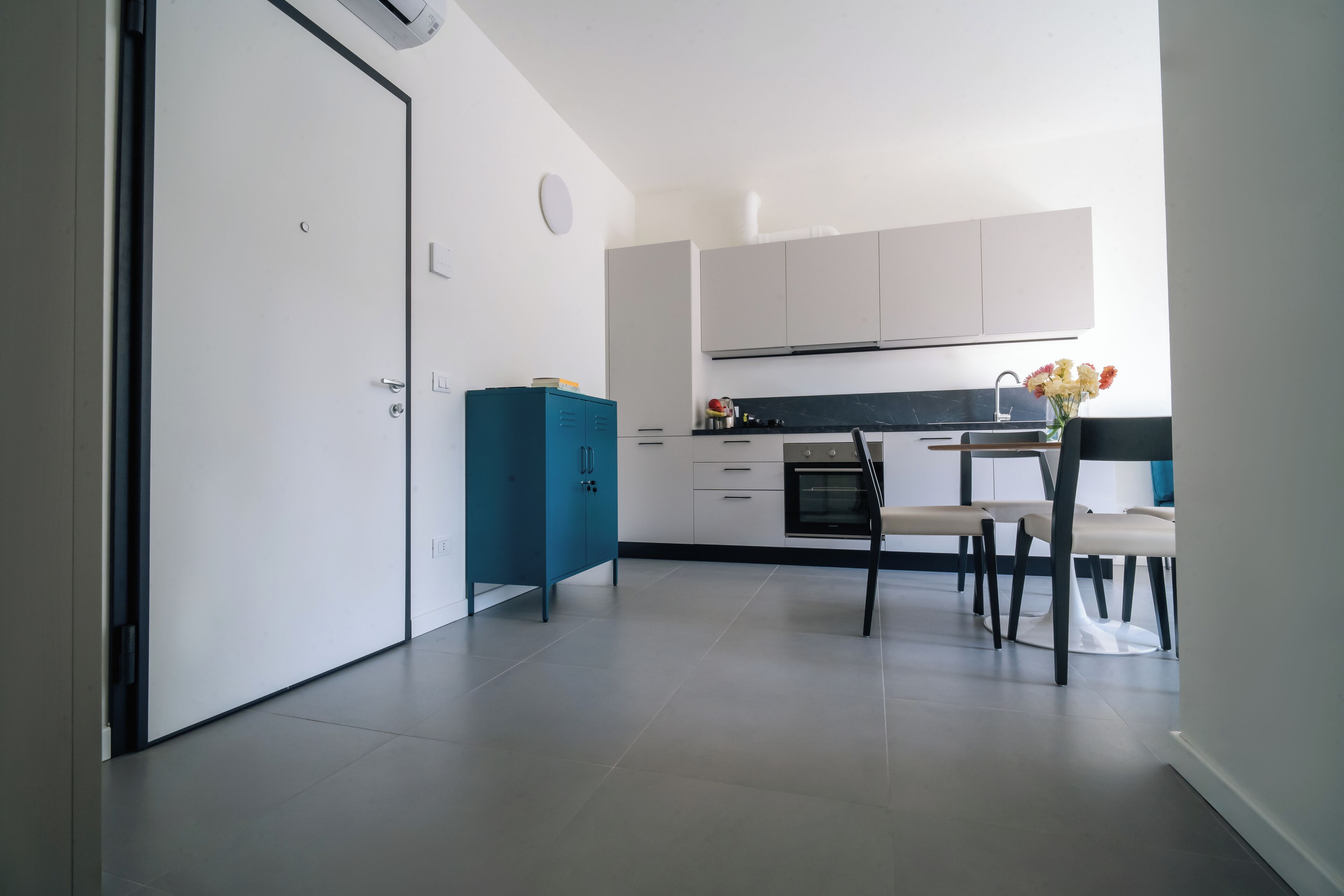 Eine moderne Küche mit weißen Schränken, einem blauen Stauraum und einem Essbereich mit Tisch und Stühlen.