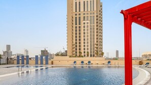 Una piscina en la azotea con agua cristalina, rodeada de sillones de descanso y un edificio alto al fondo.