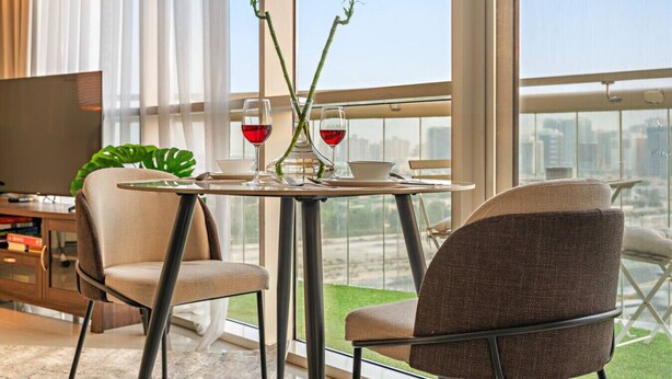 Una sala de estar moderna con una mesa de comedor, dos sillas, un televisor y un ventanal con vistas a la ciudad.
