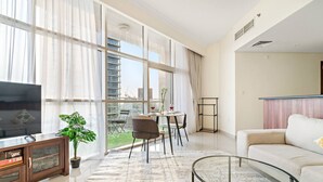 Una sala de estar moderna con un televisor grande, una mesa de centro de vidrio y un sofá. Cuenta con un comedor con una mesa y sillas, y un balcón con vistas a la ciudad.