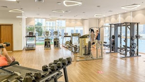 Un gimnasio con diverso equipo de ejercicio, ventanas amplias y vistas a la ciudad.