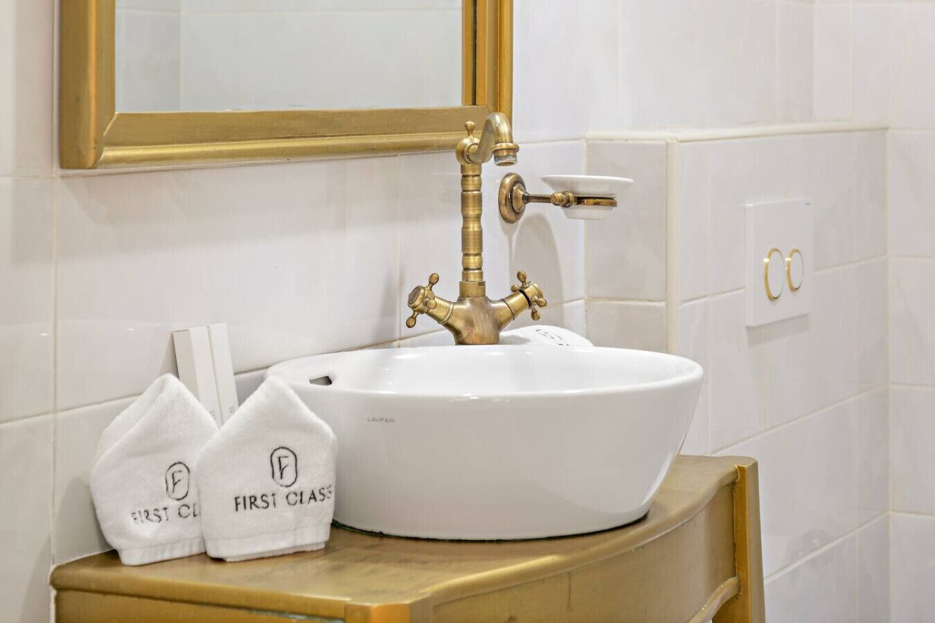 A white sink with a gold faucet in a bathroom with white tiles and gold fixtures.