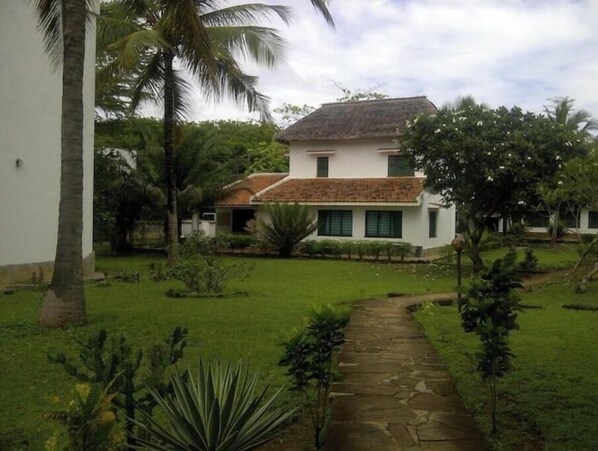 A two-story house with a thatched roof, surrounded by a well-maintained garden with a stone pathway leading to the entrance.