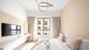 A modern hotel room with a large bed, a flat-screen TV, and a view of the city through the window. - Luxury La Mer 1BR | Balcony Sea Views + Near City Walk & Mall (Dubai)