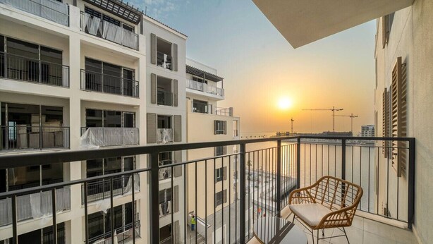 A balcony with a view of the sunset, a table with chairs, and a building with multiple balconies. - Luxury La Mer 1BR | Balcony Sea Views + Near City Walk & Mall (Dubai)